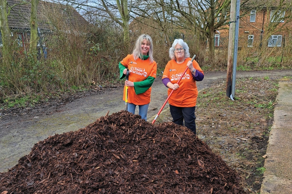 Two women in orange t-shirts standing behind a pile of bark chippings