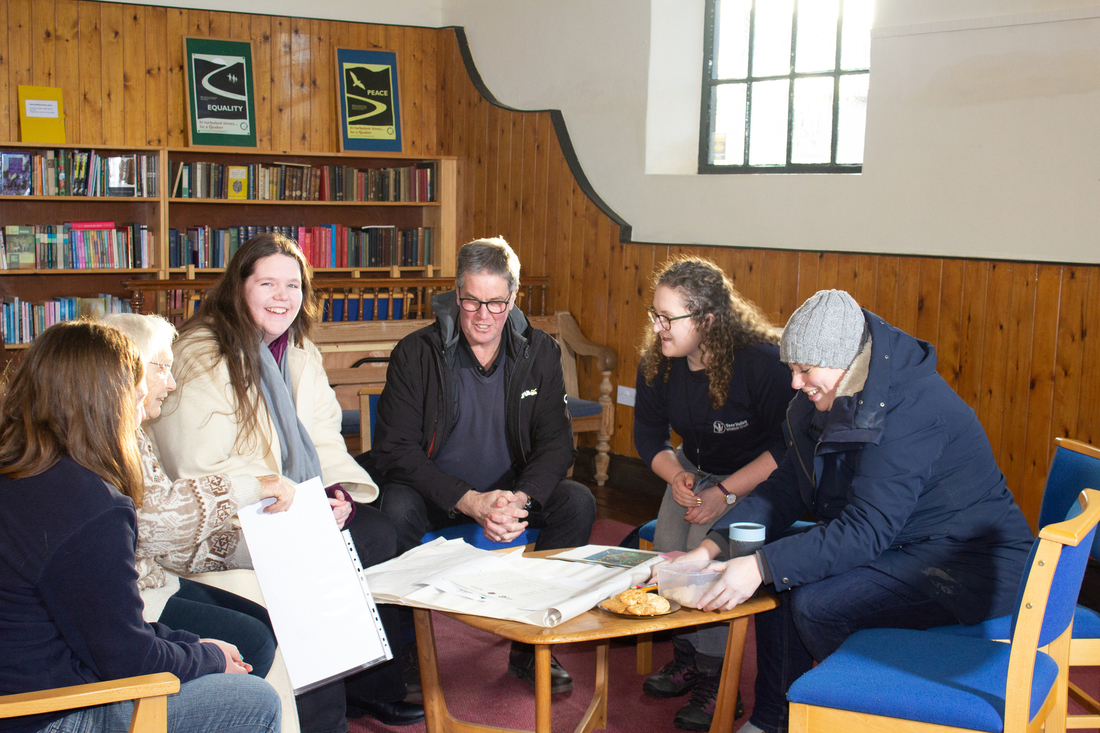 A group of people sitting around a table of paperwork inside a simple building